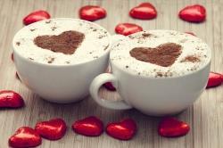 To kaffekopper pyntet med sjokoladehjerte og røde hjerter rundt
