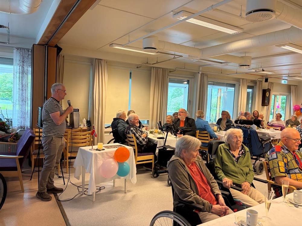 mann foran publikum i sykehjemmets aktivitetsstue - Klikk for stort bilde
