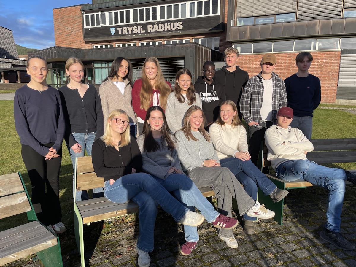 En liten gruppe tenåringer sitter og står bak to benker utenfor et rådhus - Klikk for stort bilde