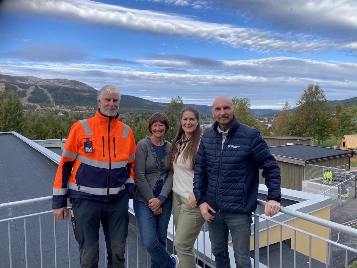 Fire voksne står ute på en veranda med ei elv og et fjell i bakgrunnen - Klikk for stort bilde