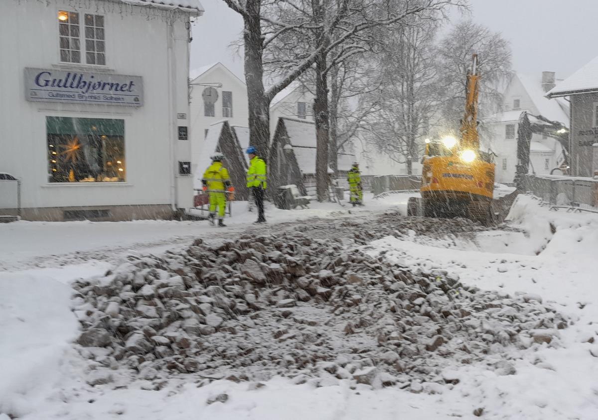 Gravemaskin og tre arbeidere i snøvær utenfor gullsmedbutikk - Klikk for stort bilde