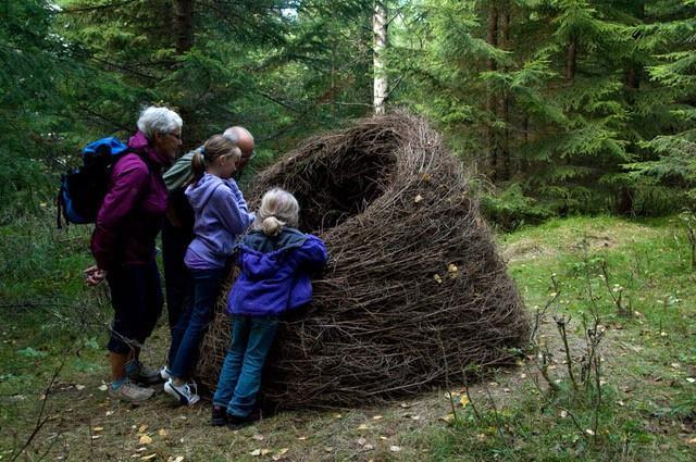To barn og to voksne står ved en stor flettet installasjon i skogen - Klikk for stort bilde