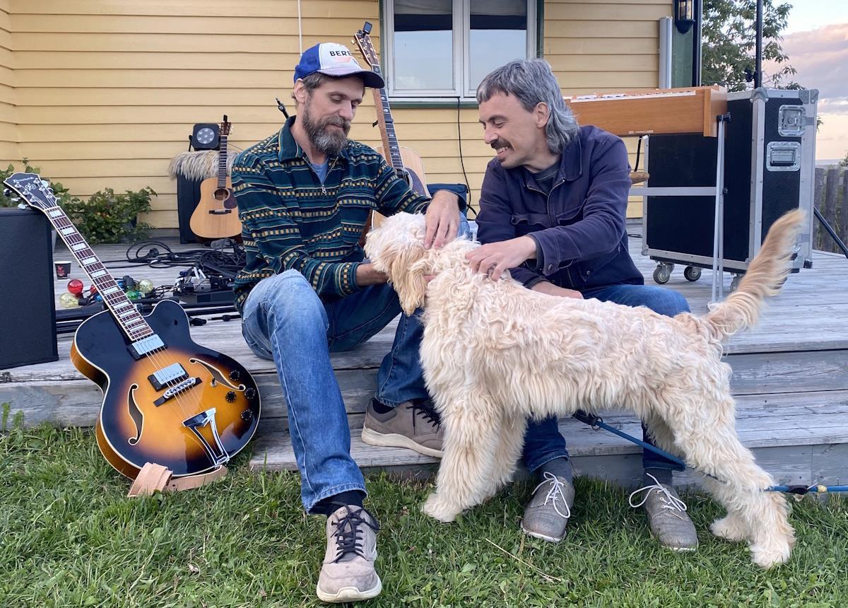 To menn sitter på en terasse og klapper en hund - Klikk for stort bilde