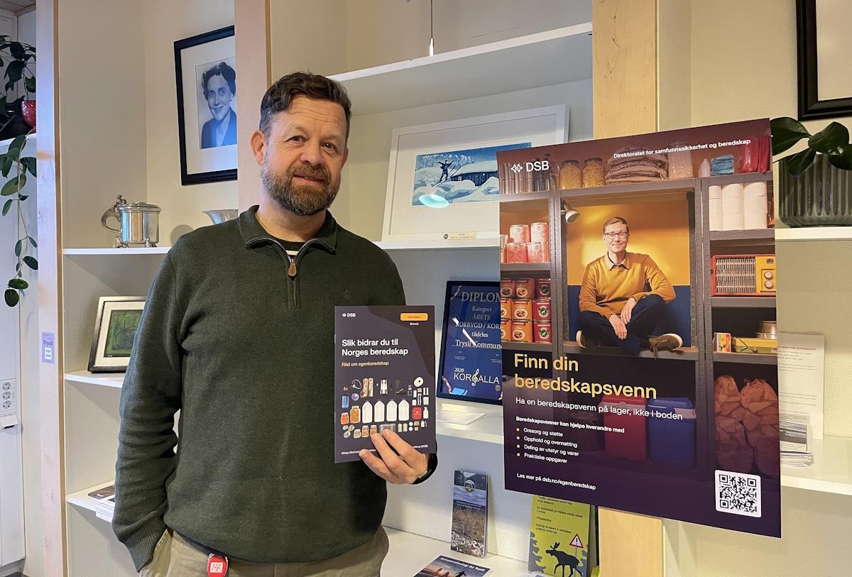 En mann holder i en brosjyre og står ved en plakat om beredskap - Klikk for stort bilde