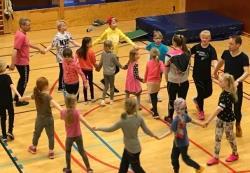 Barn danser i ring med to voksne instruktører