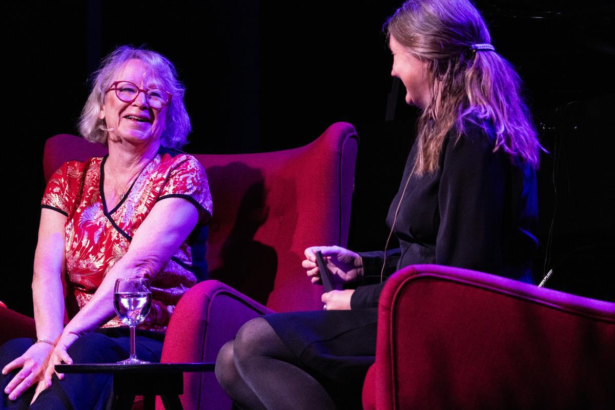 To damer som sitter i hver sin røde stol og prater. - Klikk for stort bilde