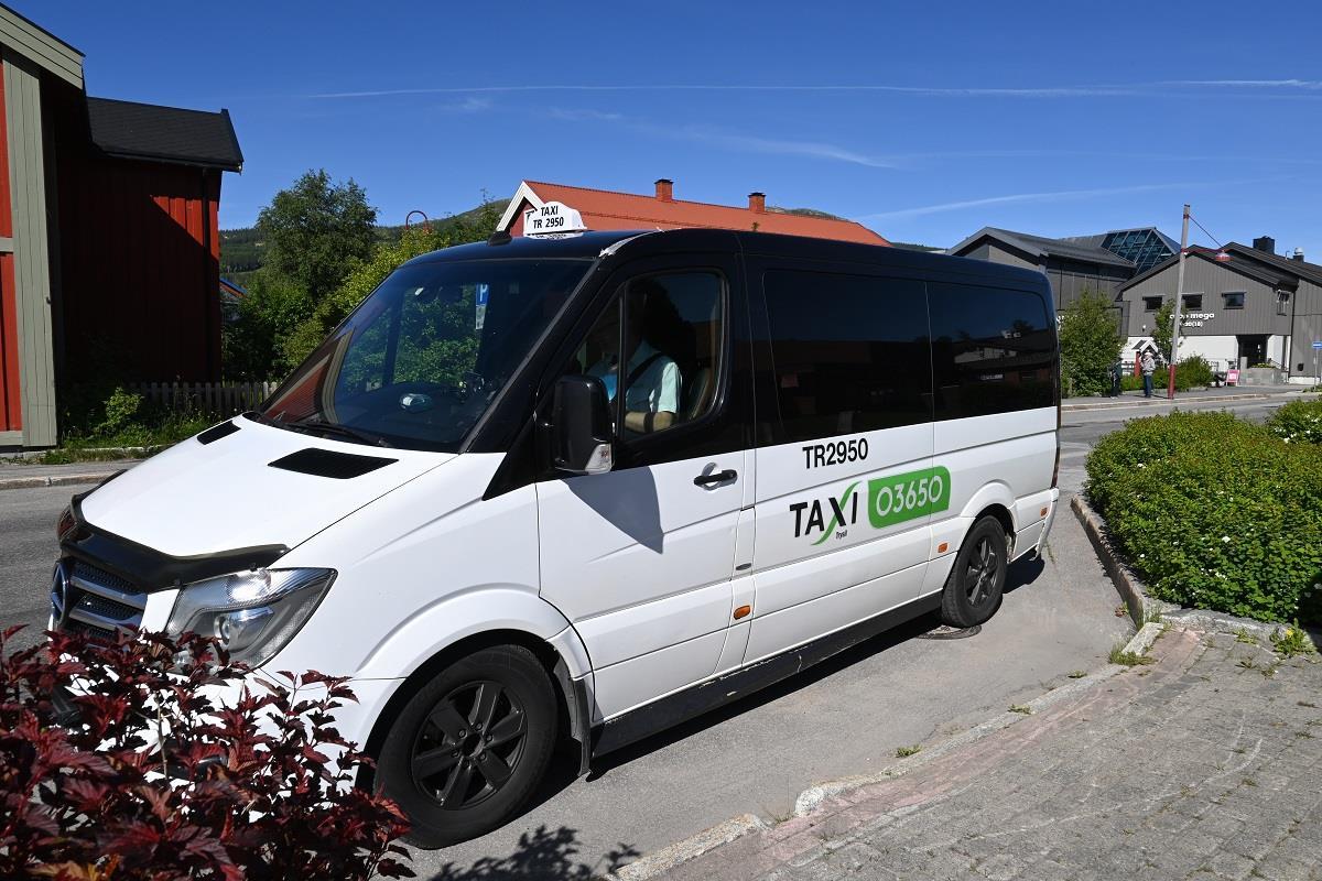 Bildet av en stor taxi som står i en busslomme i Storvegen i Trysil med kjøpesenteret i bakgrunnen - Klikk for stort bilde